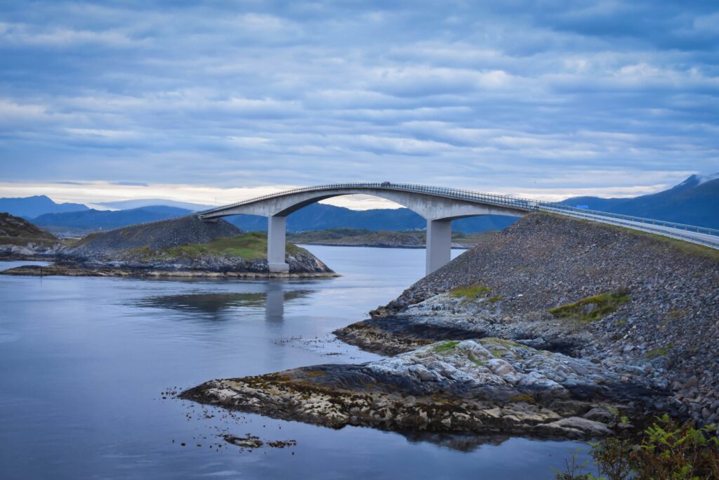 Bildet viser en bro på Atlanterhavsveien. Det er overskyet, men vindstille og vannet er rolig.