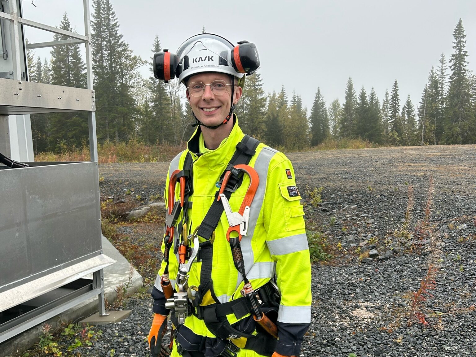 Seniorforsker, Martin Tveten står i fullt sikkerhetsutstyr på en grusslette. Han har neongul dress, hvit hjelm og sikkerhetsseler. Det er er grå, regnværsdag. Trær skimtes i bakgrunnen,