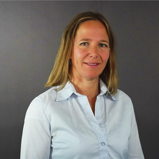 Portrettbilde av Hanne Rognebakke. Hanne er en hvit dame med mørkeblondt hår. Hun har på seg lyseblå, langermet skjorte.