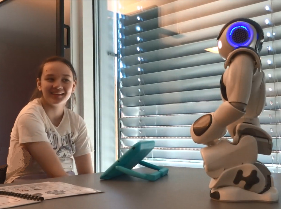 «Sol» smiler mot roboten som sitter på huk på pulten hennes