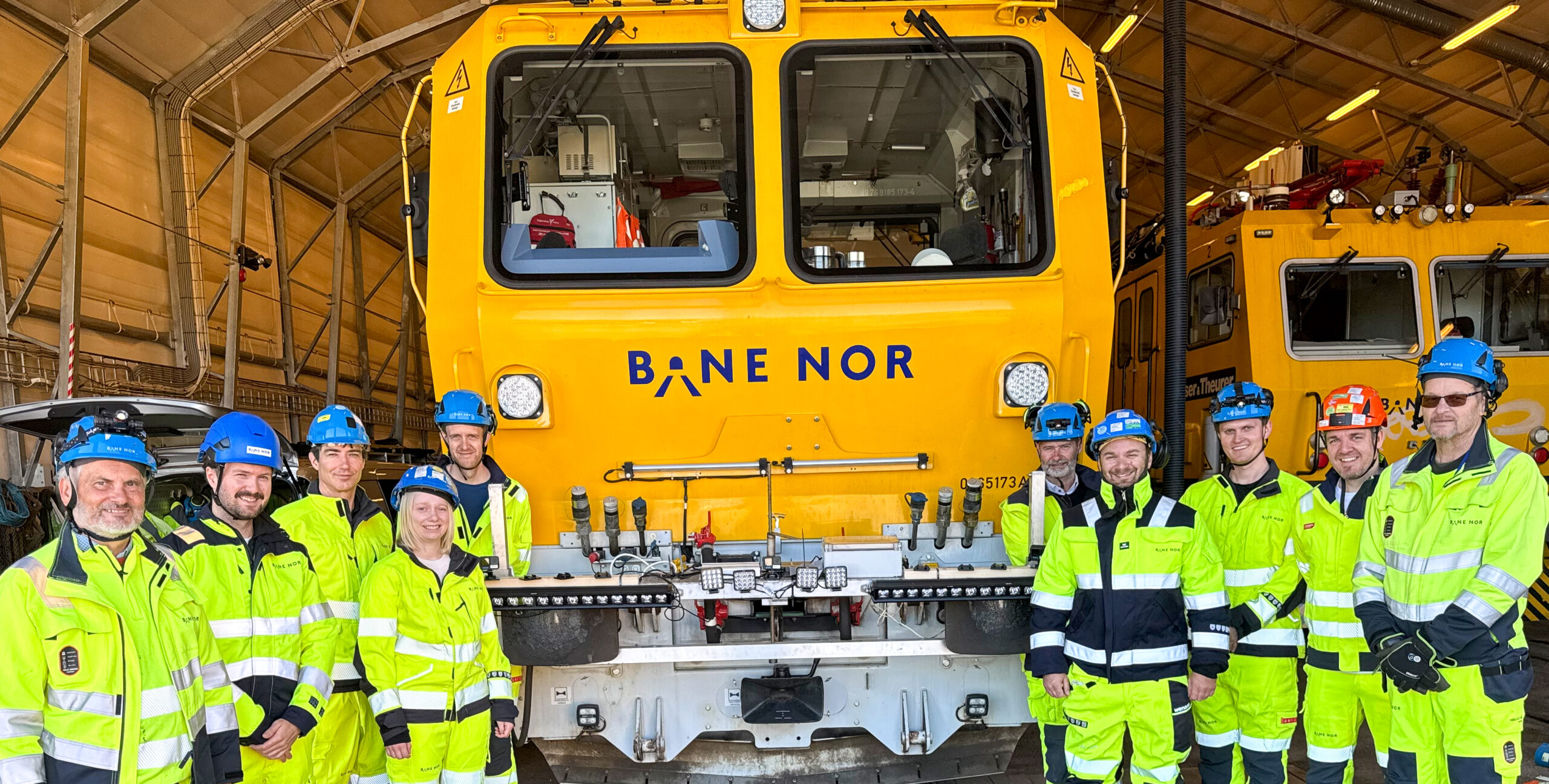 Bildet viser forskere og fagfolk fra NR og Bane NOR i fullt verneutstyr foran et av Bane NORs inspeksjonstog. Toget er gult.