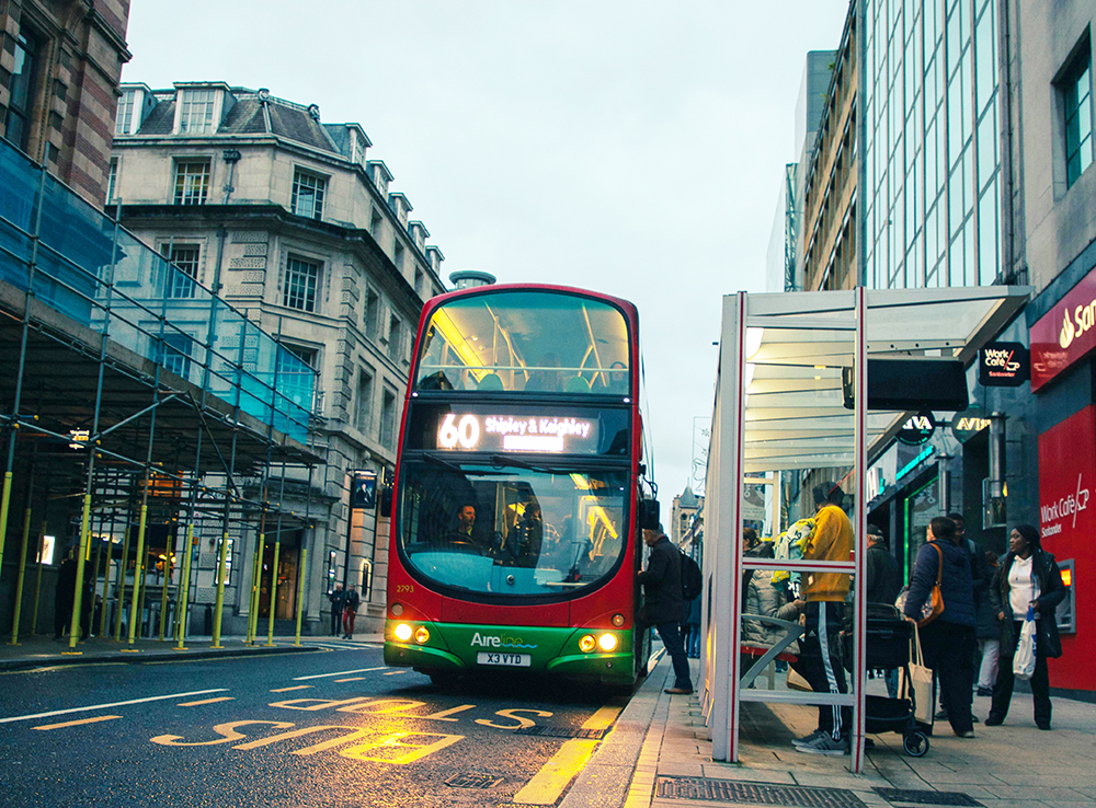 Gate med buss som står på holdeplass og mennesker som går på