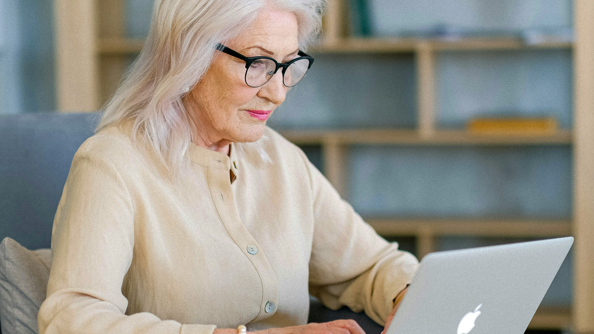 En eldre dame sitter ved laptopen sin, Hun sitter på en sofa og har på seg briller