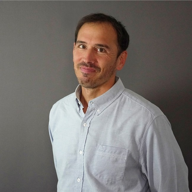 Mann med mørkt hår og blå skjorte i portrett.