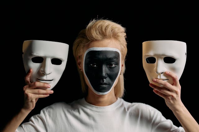 Skuespiller med ansiktsmaling holder opp to masker, en på hver sider av ansiktet
