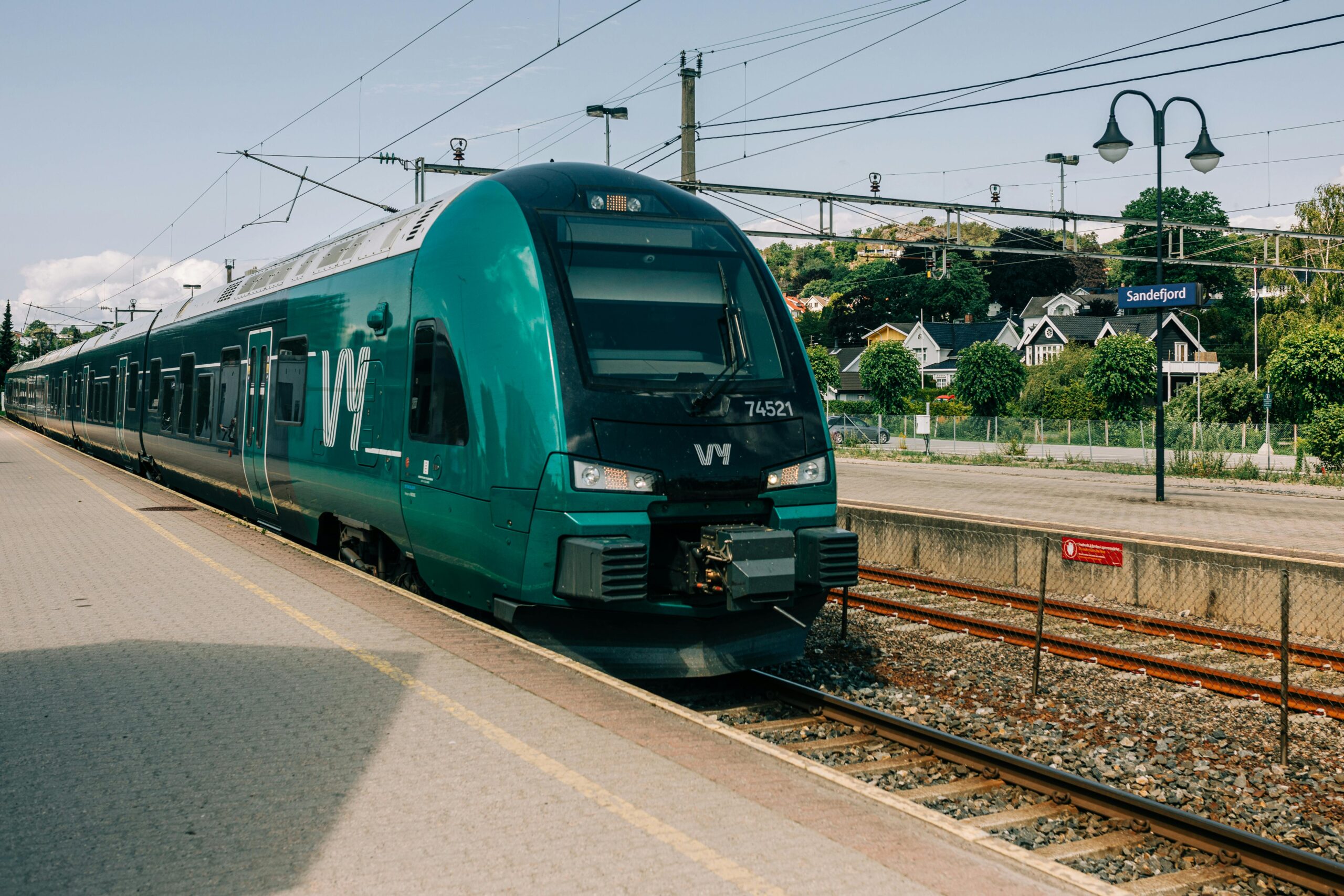 The image shows a green Vy train in Norway, which has come to a halt at Sandefjord station.
